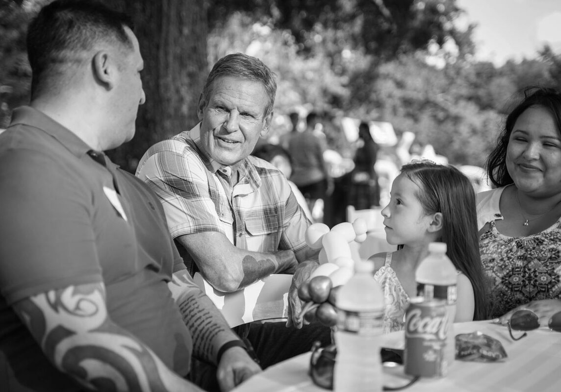 a diverse family at a blue star families neighborhood event sharing a table, meal and conversation with local government official